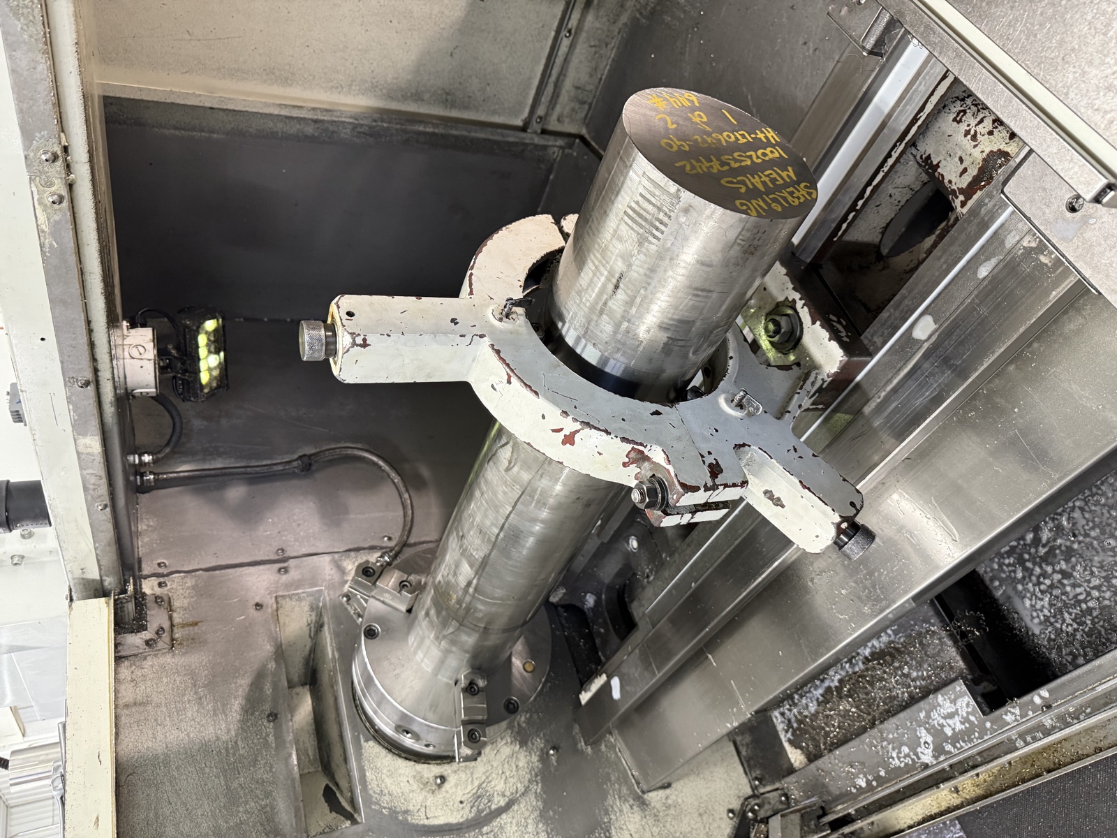 A long steel bar in the CNC lathe chuck, held by a steady rest